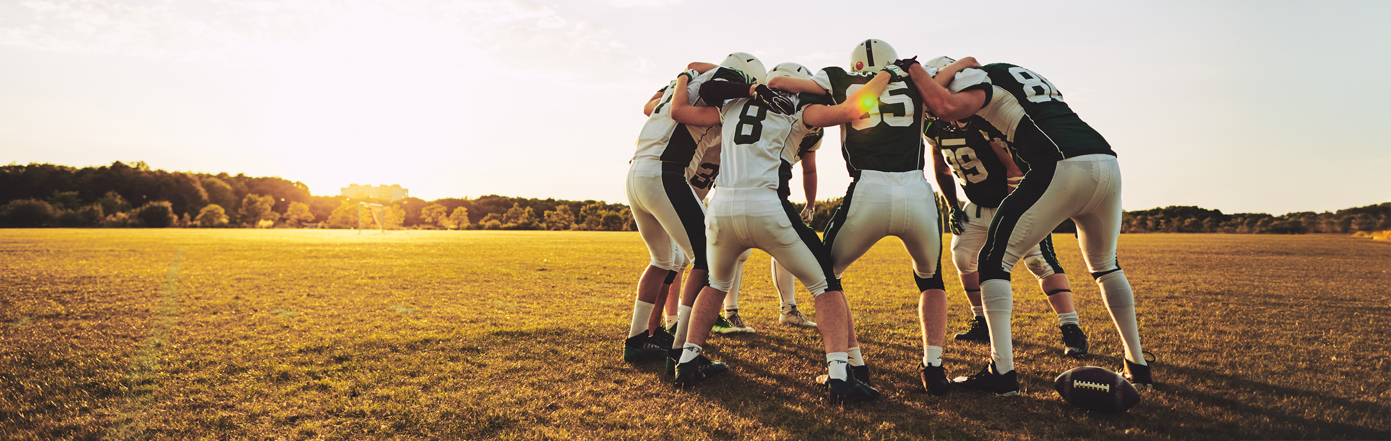 Group of young American football players standing in a huddle together on a sports field in the afternoon discussing before a game