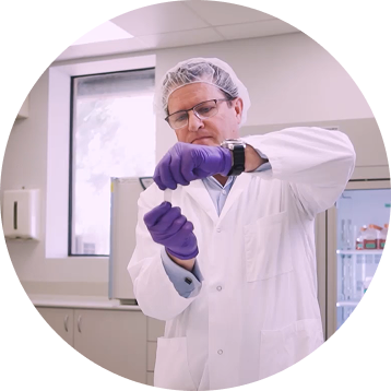 Scientist in white lab coat, safety glasses and purple gloves handling a medical sample in a sterile laboratory environment