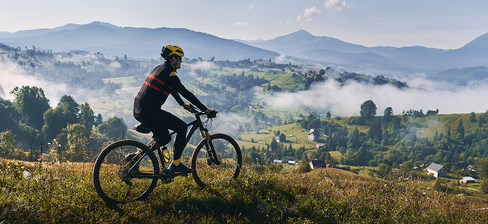 Mountain biker riding through a scenic alpine landscape with misty valleys and rolling hills in the background, representing an active lifestyle and physical recovery