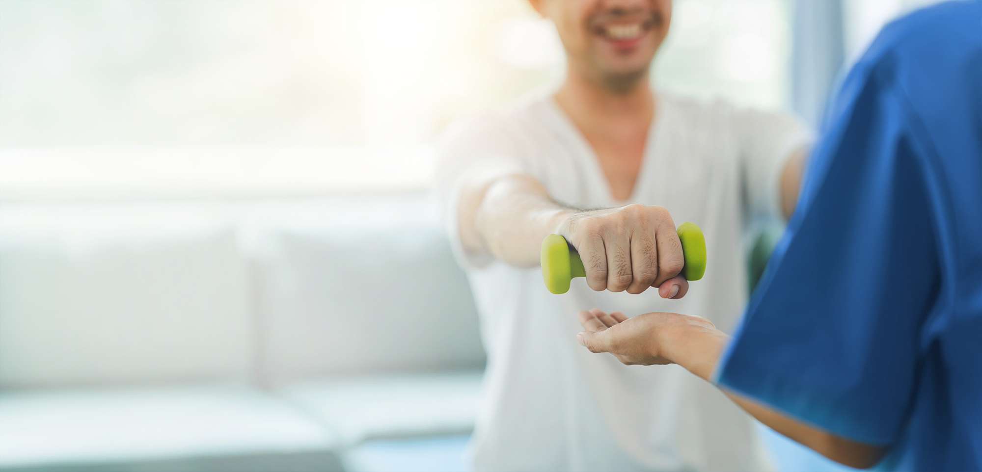 Smiling patient performing arm strength rehabilitation exercise with a dumbbell under the guidance of a physiotherapist in a clinical setting