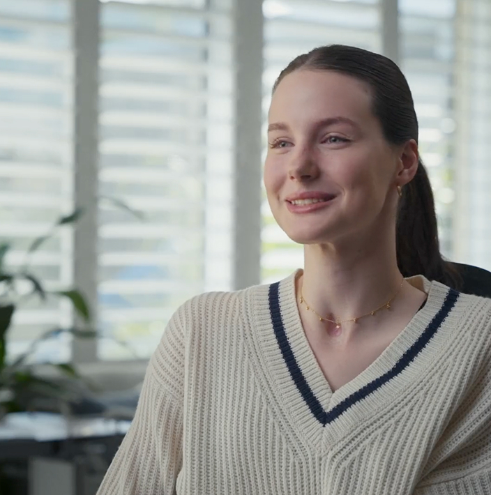Young woman smiling during an interview in a bright modern office environment with window blinds and indoor plants in the background