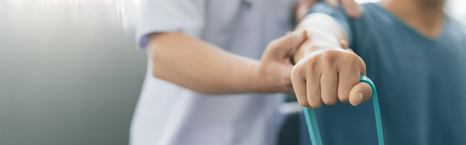 Healthcare professional supporting a patient's arm during a resistance band rehabilitation exercise in a clinical setting