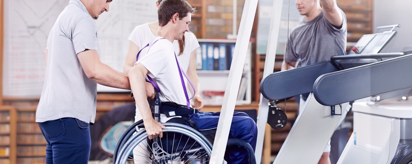 Physical therapist assisting a young patient in a wheelchair during a rehabilitation session in a physiotherapy clinic with exercise equipment