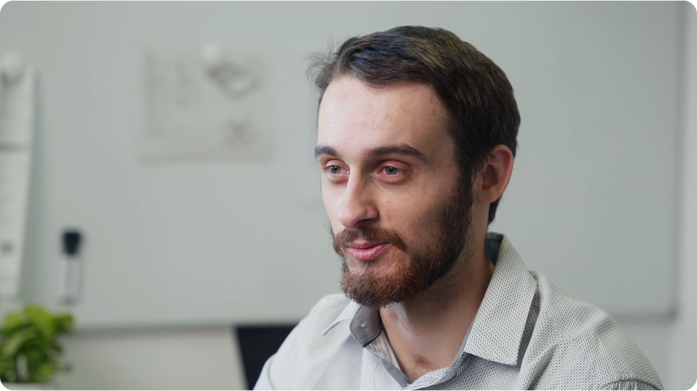 Liam Shepherd speaking during a video testimonial interview in a modern office setting with a whiteboard in the background
